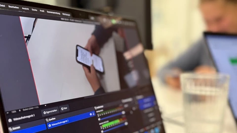 Auf einem Notebook-Bildschirm ist zu sehen, wie eine Person ein Smartphone bedient