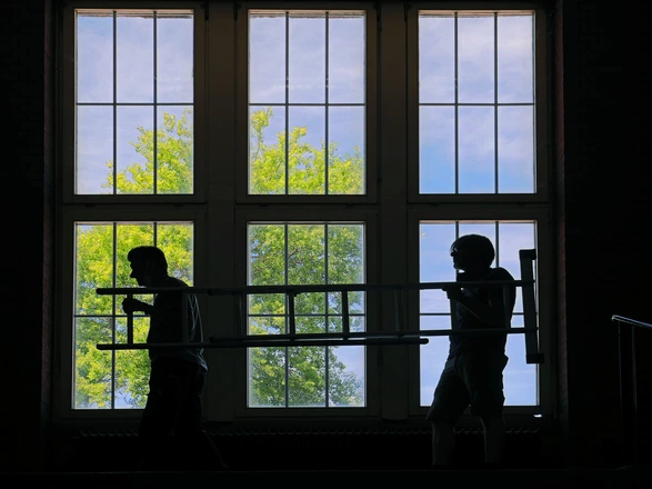 Ein Silhouetten-Bild zweier Handwerker vor einem großen Fenster der Zeche 