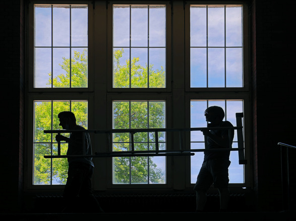 Ein Silhouetten-Bild zweier Handwerker vor einem großen Fenster der Zeche